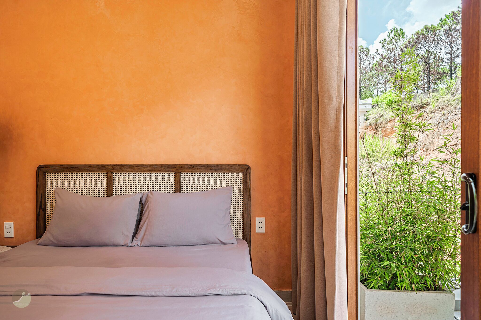 A bedroom with a bed, a wooden headboard, and a view of greenery outside.