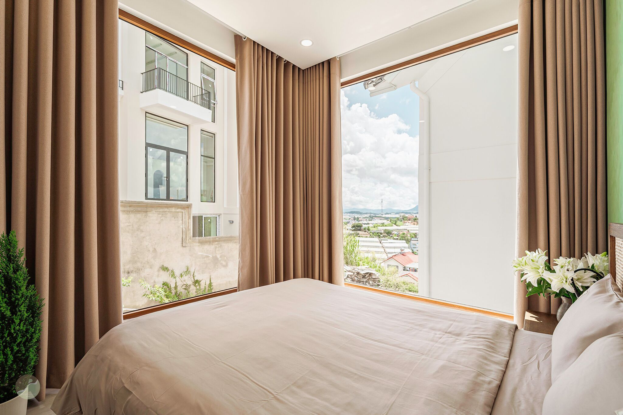 Ein Schlafzimmer mit einem großen Bett, Blick auf ein Gebäude und einem Balkon mit Pflanzen.