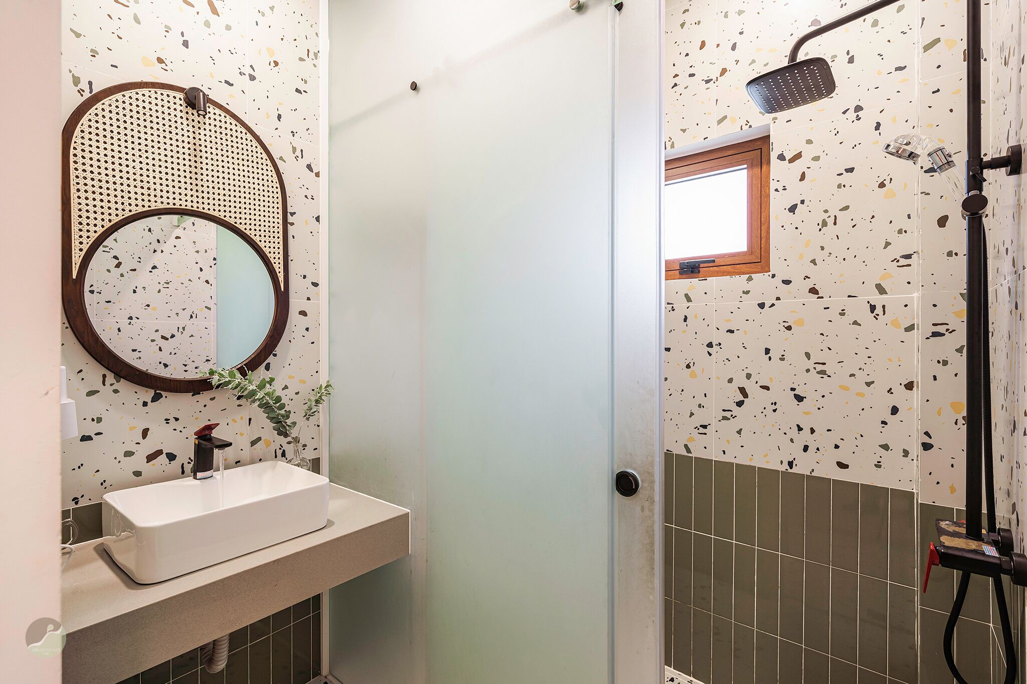 Une salle de bain avec un miroir rond, un lavabo rectangulaire et une douche équipée d’un pommeau de douche à main.