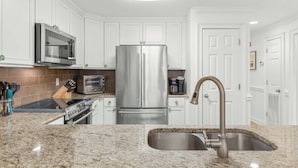 A modern kitchen with white cabinetry, stainless steel appliances, a granite countertop, and a built-in oven. - Brass Rail 106 | Enjoy an Easy Stroll to the Beach or Pool! (Tybee Island)