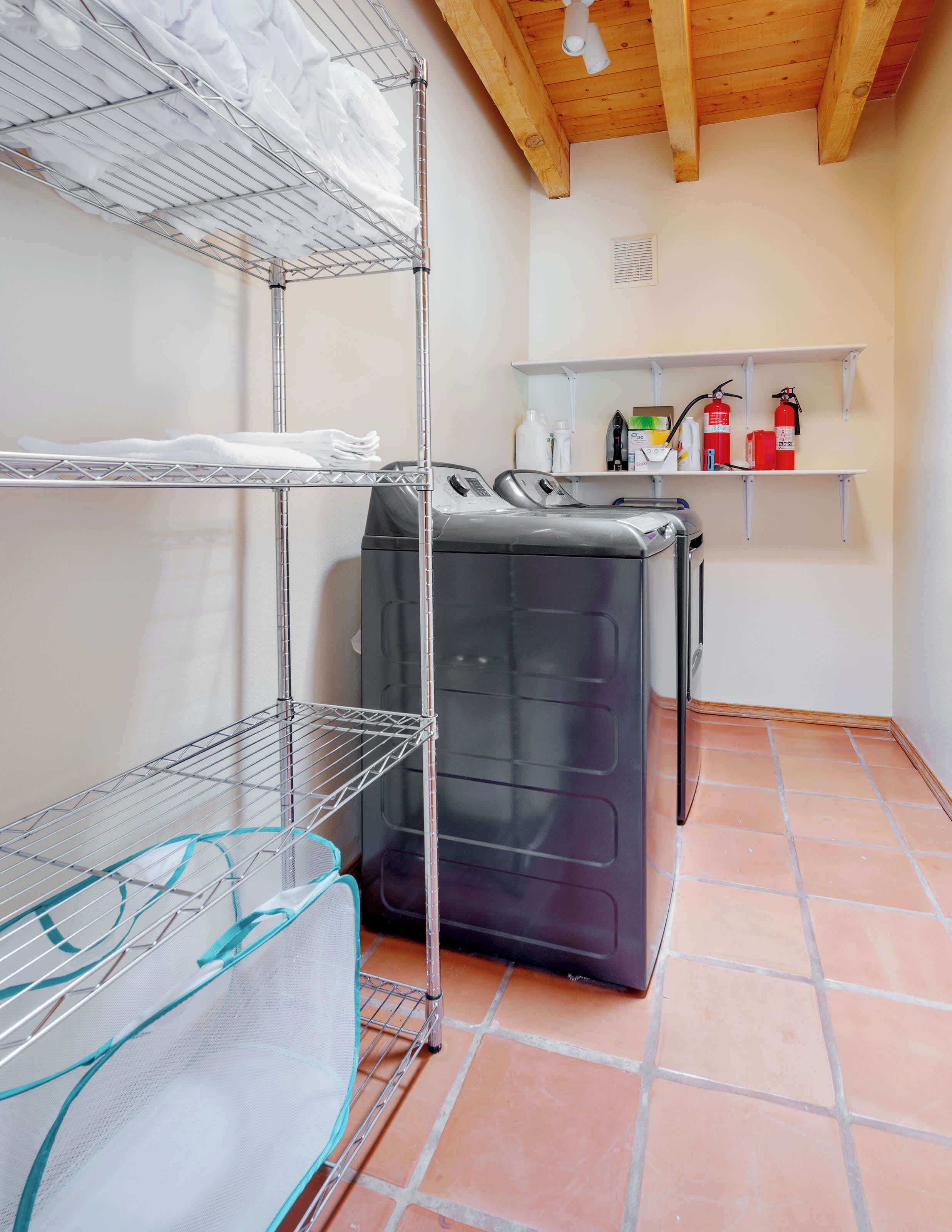 Un cuarto de lavandería con dos lavadoras apiladas, estantes metálicos para secar ropa y repisas con útiles de limpieza.