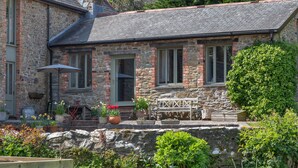 Une maison en pierre avec un jardin, un banc et des plantes en pot.