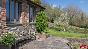 Un bâtiment en pierre, avec un banc et des plantes en pot au premier plan.
