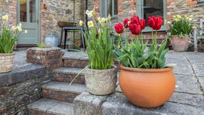 Un bâtiment en pierre avec un escalier en briques, des plantes en pot et une table avec un parasol.