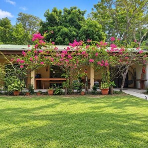 A building with a covered patio area, surrounded by a well-maintained lawn and various potted plants. - Villas Playa Palo Seco (Parrita)