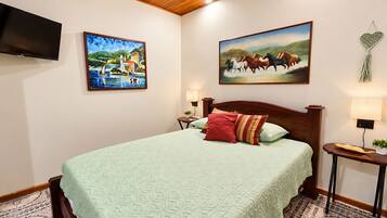 Een hotelkamer met een bed, twee schilderijen, een televisie, een nachtkastje en een lamp.