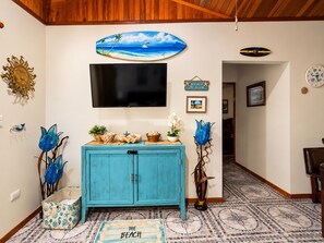 Una habitación con un mueble azul verdoso, un televisor de pantalla plana, decoración en la pared y un suelo estampado.