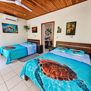 Una habitación con dos camas, cada una con una colcha estampada con tortugas marinas, un ventilador de techo y una puerta que da a un baño.