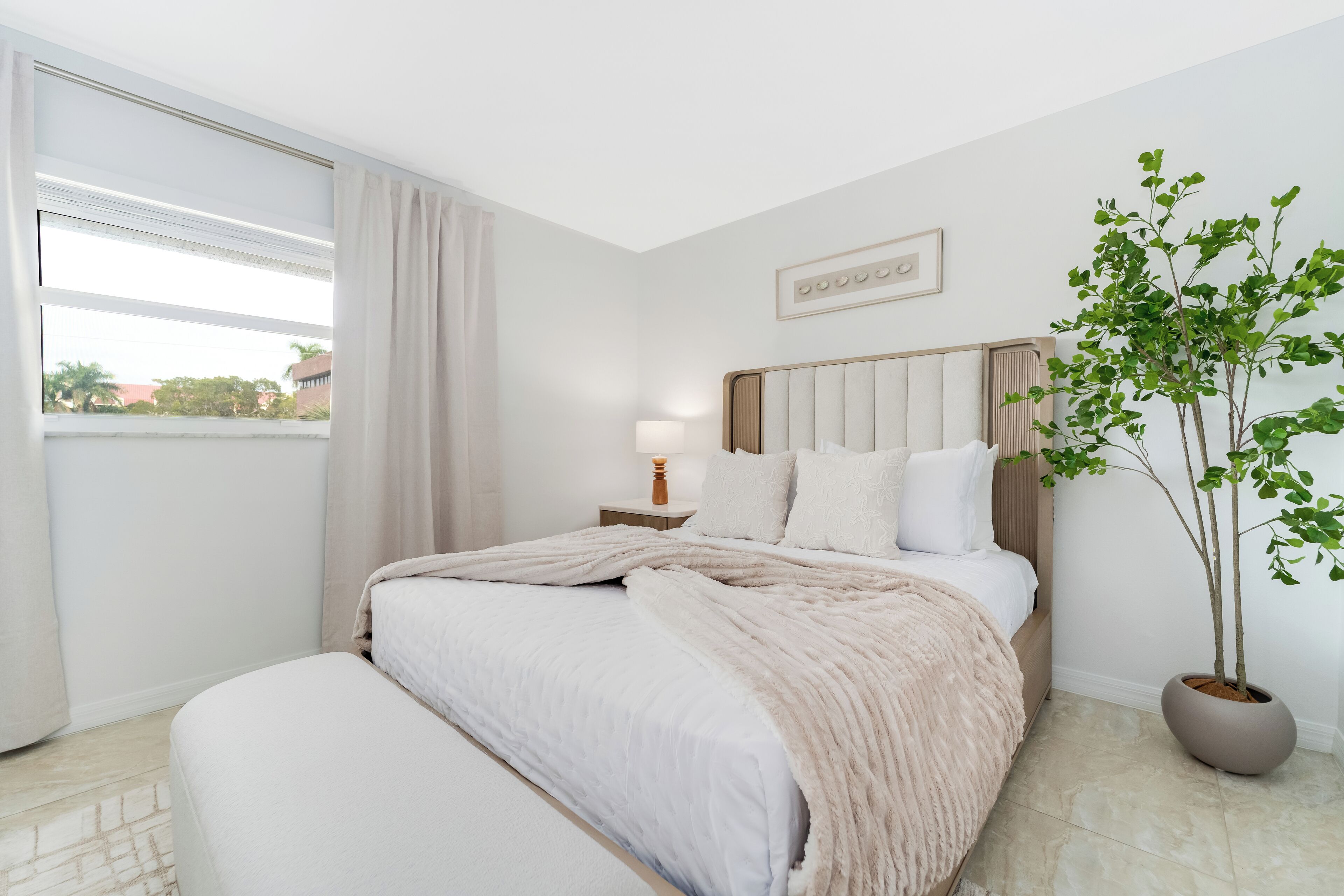 A bedroom with a bed, bedside table, lamp, and a potted plant.