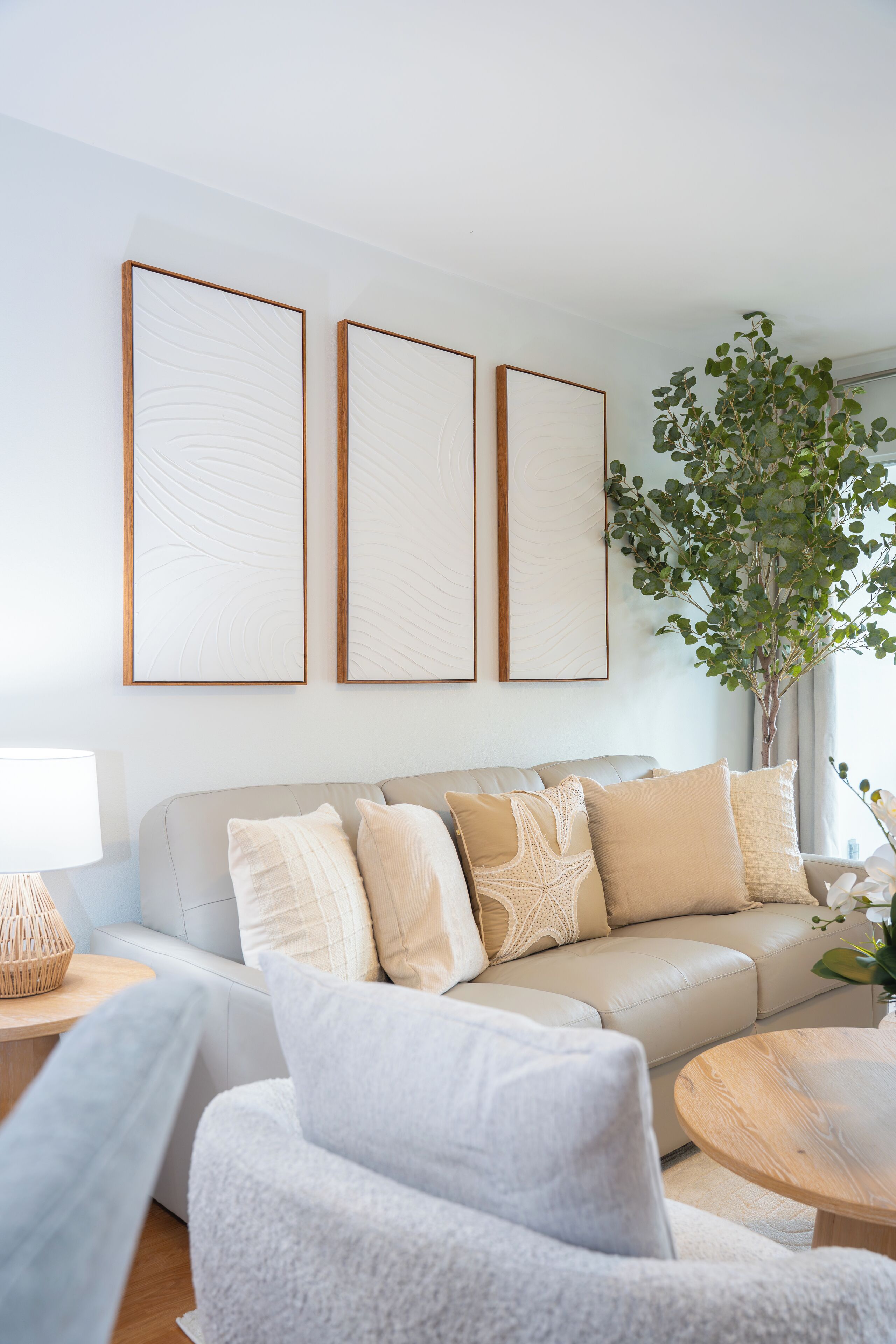 A modern living room with a beige sofa, a round wooden coffee table, and a large potted plant.
