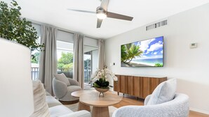 Ein modernes Wohnzimmer mit einem weißen Sofa, grauen Sesseln, einem Holztisch und einem großen Fernseher, der an der Wand montiert ist.