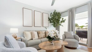 Ein modernes Wohnzimmer mit einer Couch, Sesseln, einem Couchtisch und einem großen Fenster mit Blick ins Freie.