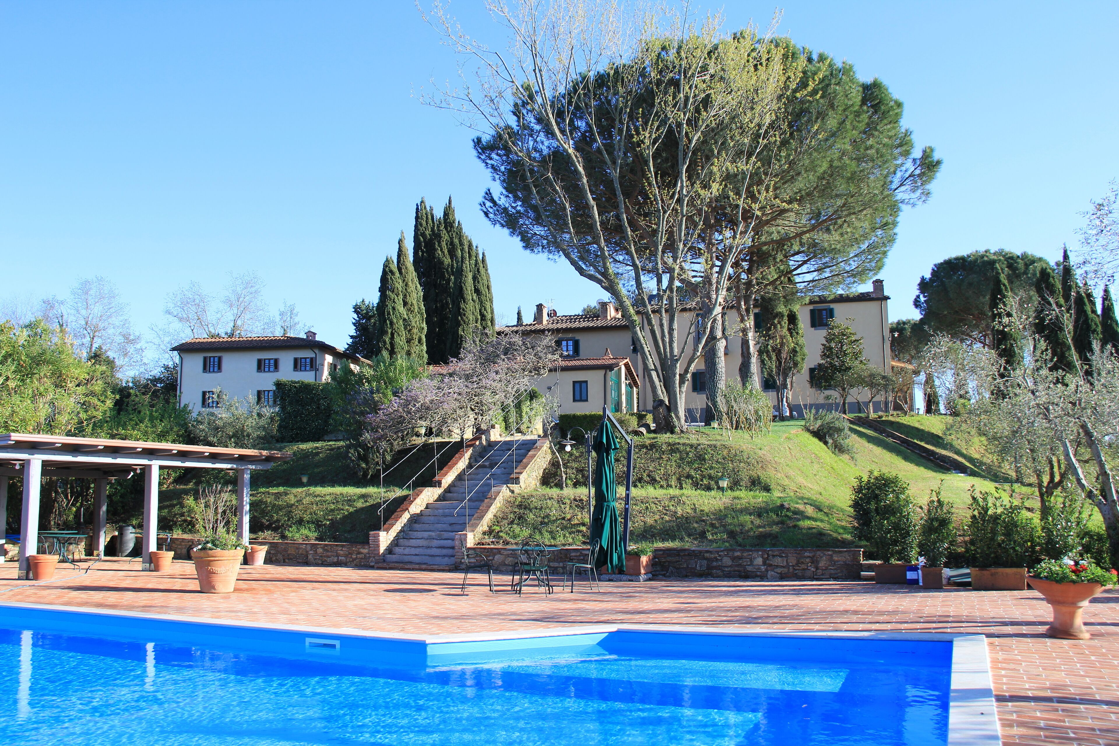 Ein Swimmingpool mit Terrassenbereich, Treppen, die zu einem Gebäude führen, und umgebender Bepflanzung.