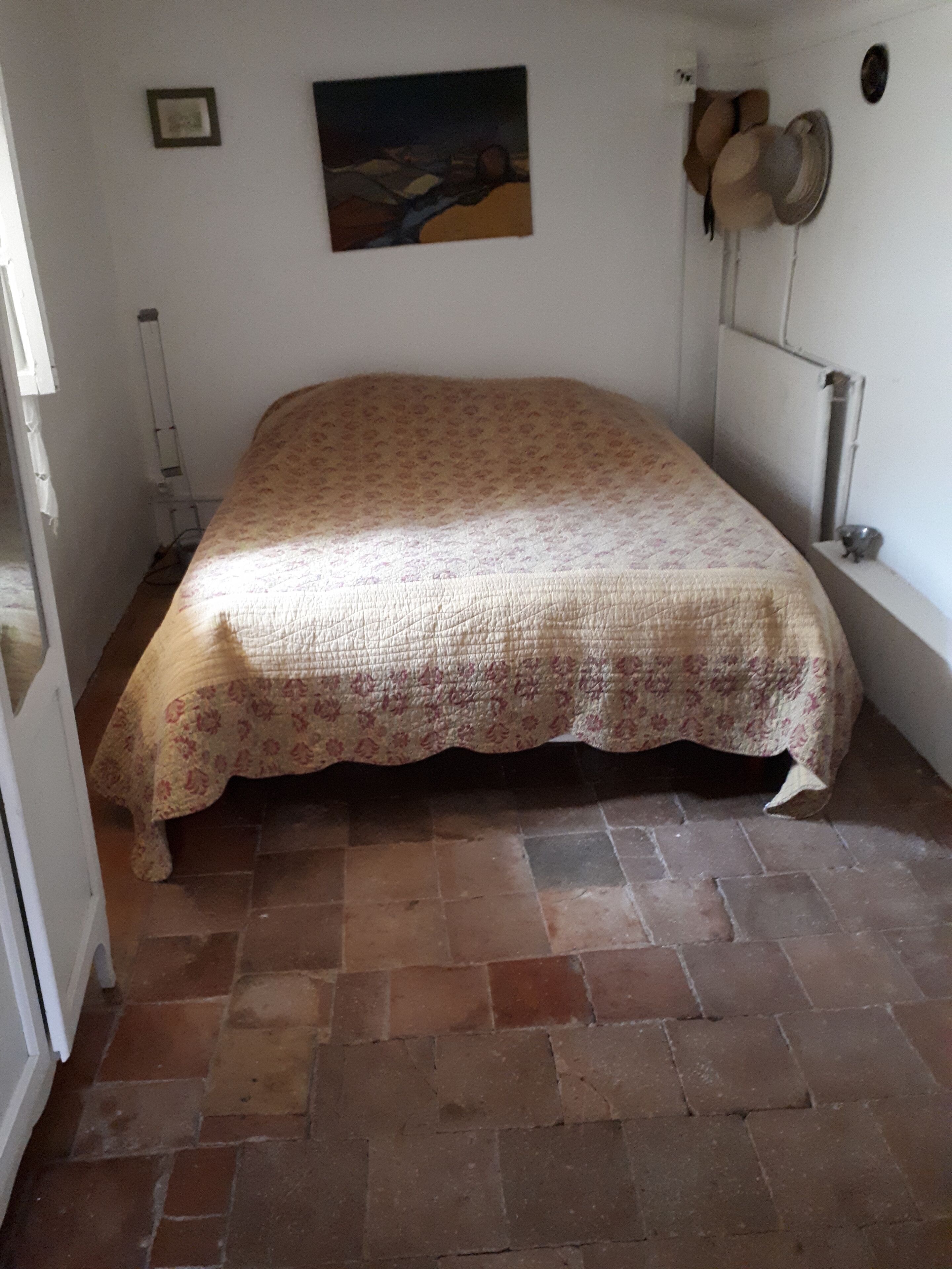A bedroom with a bed, a painting on the wall, and a radiator.