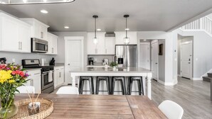 Una cocina moderna con gabinetes blancos, electrodomésticos de acero inoxidable y una isla central con taburetes de bar.