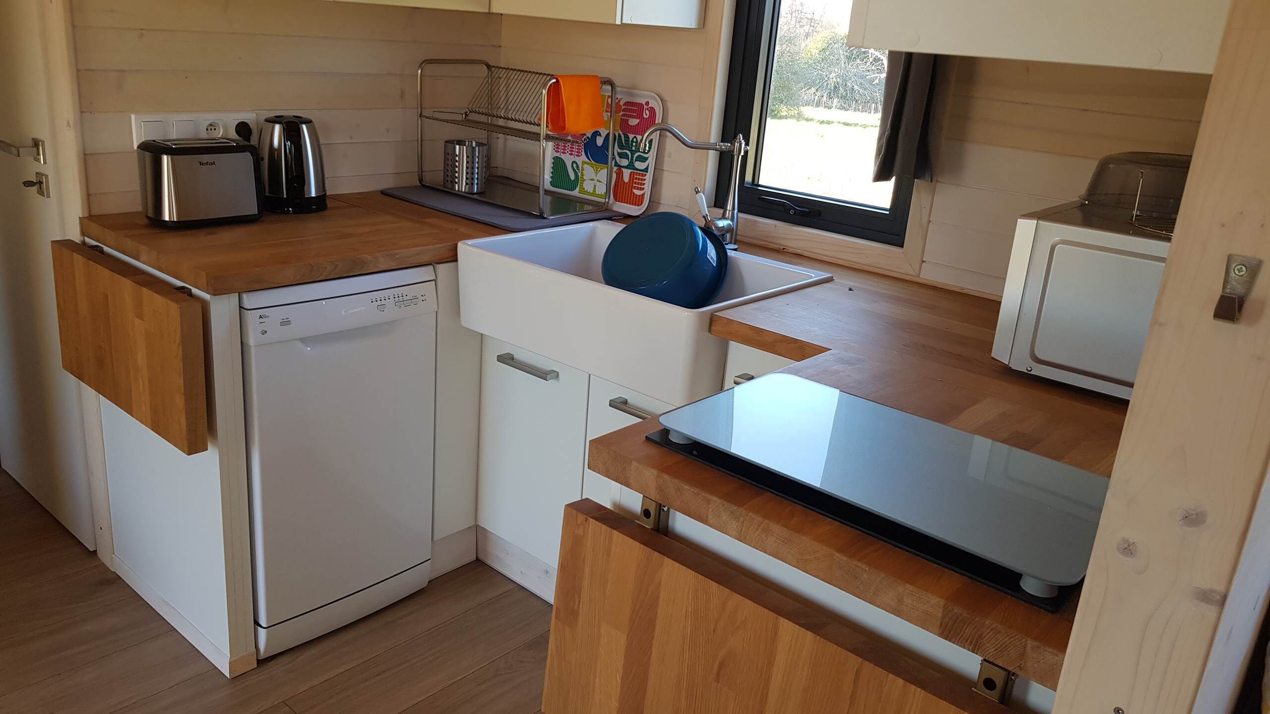A compact kitchen with a dishwasher, toaster, kettle, and a small refrigerator.
