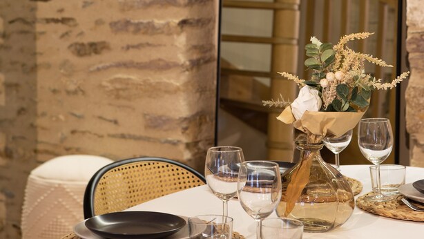 A dining table set with plates, glasses, and a vase of flowers, with a stone wall and wooden staircase in the background. - L'Honoré - Appt T2 en duplex - centre ville (Rennes)