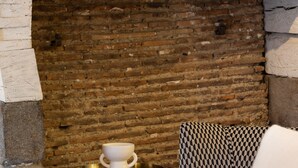 A room with a brick wall, a patterned sofa, a small table with a white bowl, and a wooden chair. - L'Honoré - Appt T2 en duplex - centre ville (Rennes)