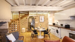 A cozy living area with a dining table, chairs, and a sofa. A staircase leads to an upper level. - L'Honoré - Appt T2 en duplex - centre ville (Rennes)