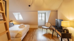 A bedroom with a bed, a desk with a television, a chair, and a lamp. There are windows and a ceiling light. - L'Honoré - Appt T2 en duplex - centre ville (Rennes)