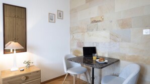 Une petite pièce avec un meuble en bois, un bureau avec un ordinateur portable, deux chaises, une lampe et un mur orné de motifs en mosaïque.