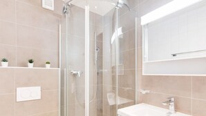 Une salle de bain moderne avec une douche à parois de verre, un lavabo blanc et un miroir au-dessus du lavabo.