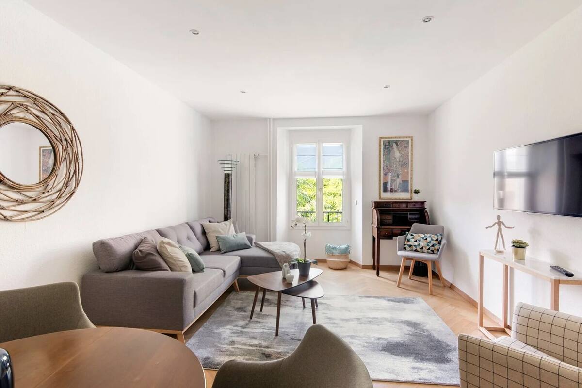 Un salon moderne avec un canapé d’angle gris, une table basse ronde et un téléviseur fixé au mur.