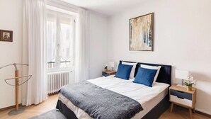 Une chambre moderne avec un grand lit, des rideaux blancs, un radiateur, une lampe sur pied et un tableau encadré au mur.