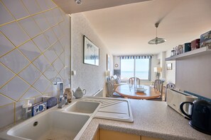 A modern kitchen with a large sink, a dining area with a table and chairs, and a view of the beach through the window.