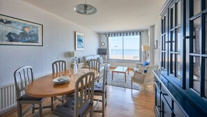 A dining area with a wooden table, chairs, and a view of the beach through large windows. - Duplex Etoile de mer- T4 Vue mer (Courseulles-sur-Mer)