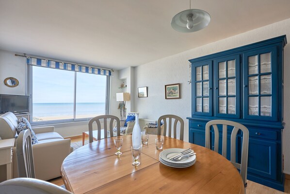 A dining area with a wooden table, chairs, and a view of the beach through large windows.