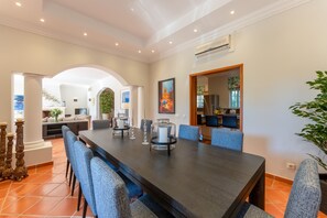A spacious dining area with a long table, blue upholstered chairs, and decorative candle holders. - Villa Breena - Quinta do Mar (Quinta do Lago)
