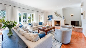 A spacious living room with a sofa, armchairs, a coffee table, and a fireplace. - Villa Breena - Quinta do Mar (Quinta do Lago)
