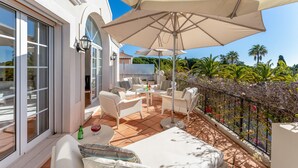 A sunlit outdoor patio with white wicker furniture, large umbrellas, and a view of palm trees. - Villa Breena - Quinta do Mar (Quinta do Lago)