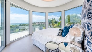 Een moderne slaapkamer met een groot bed, twee stoelen, een ronde tafel en uitzicht op de oceaan.