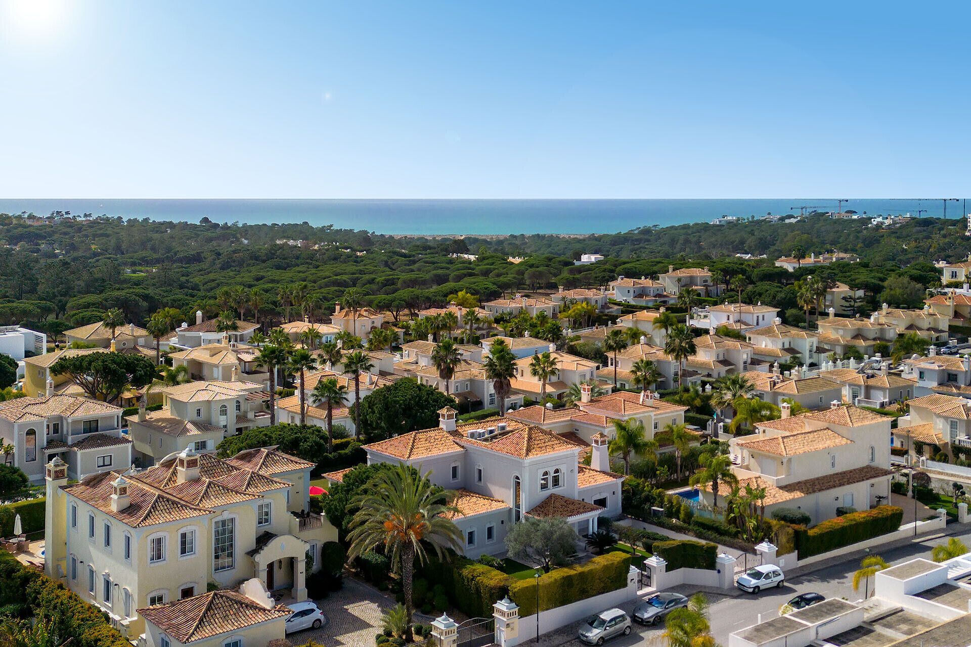 A coastal residential area with terracotta-roofed houses, lush greenery, and a clear view of the sea.