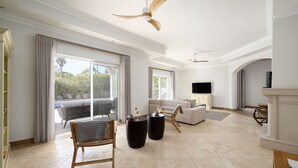 A spacious living room with a large window, a sofa, a coffee table, and a television. - Villa Flamingo - Quinta do Mar  (Vale do Lobo)
