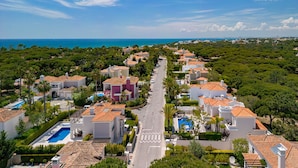 A coastal residential area with houses featuring terracotta roofs, a central road, and a view of the sea. - Villa Flamingo - Quinta do Mar  (Vale do Lobo)