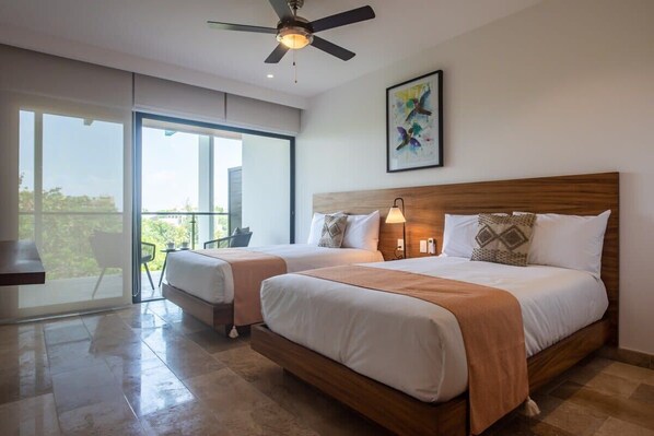 A hotel room with two beds, a ceiling fan, a large window with a view, and a painting on the wall.
