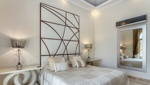 A modern bedroom with a large bed, bedside tables, a decorative wall panel, and a large mirror.