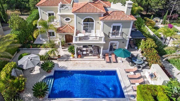 A large, luxurious villa with a swimming pool, outdoor seating, and lush landscaping.