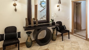 A spacious foyer with a large mirror, two black chairs, a console table, and a decorative floor pattern.