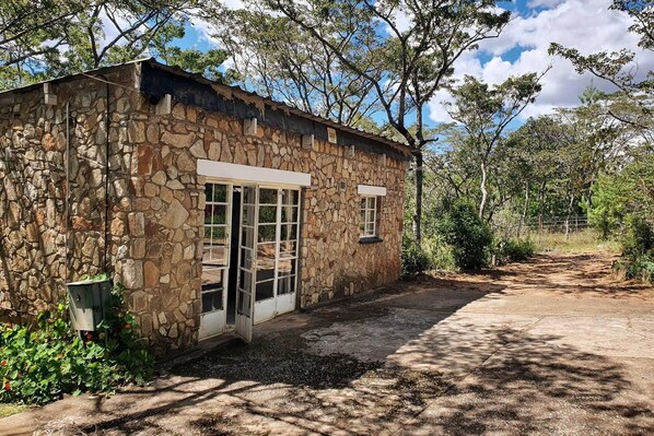 A stone building with a dirt path leading to it, surrounded by trees and vegetation.