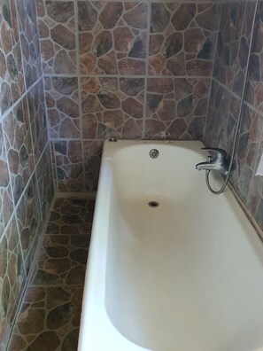 A bathroom with a white bathtub, stone wall tiles, and a showerhead.