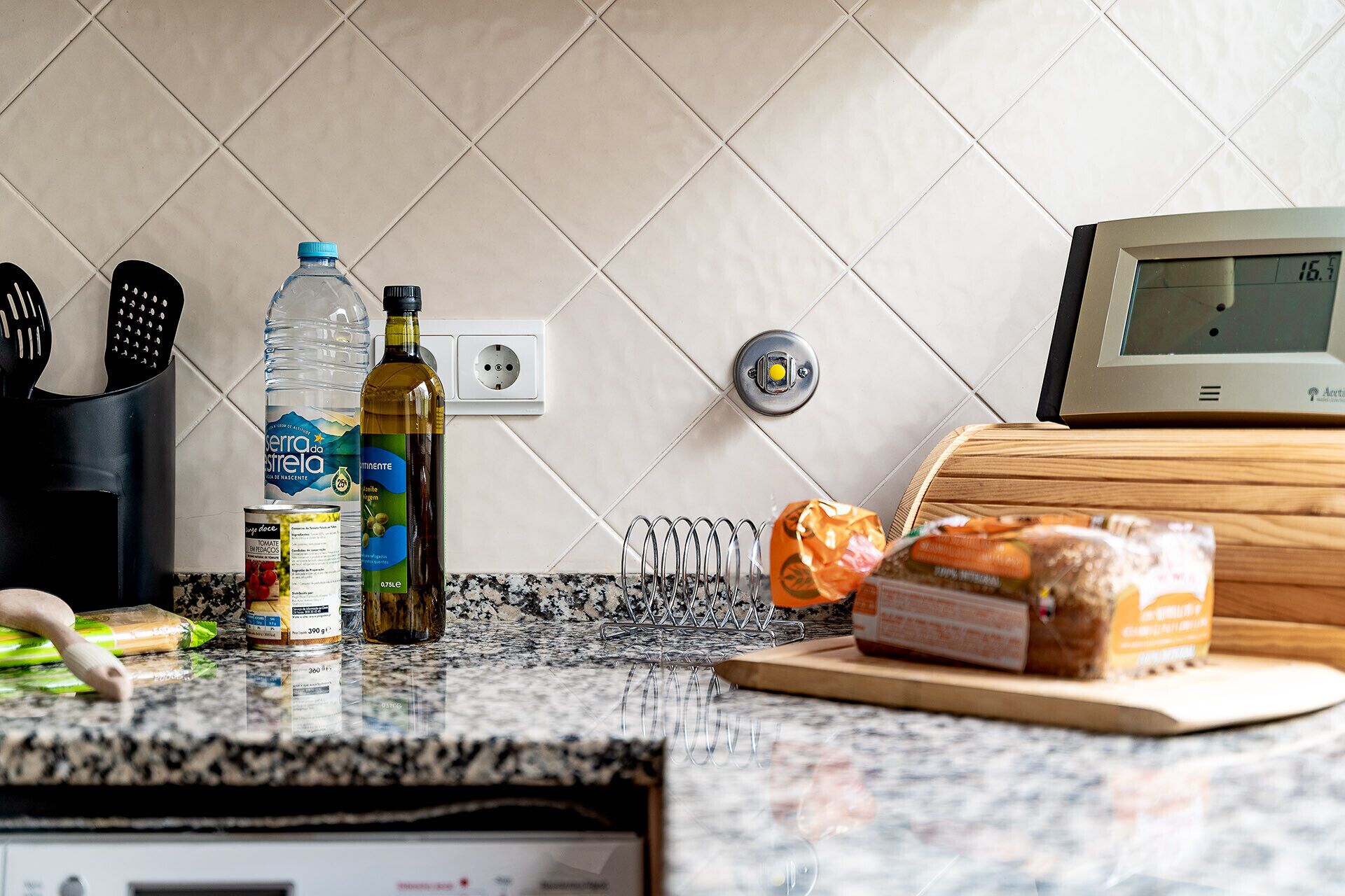 A kitchen counter with a water bottle, olive oil, bread, and a cutting board.