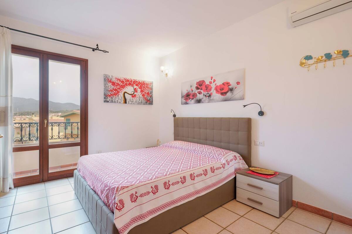Une chambre à coucher comprenant un lit, une table de chevet, une fenêtre avec vue et deux œuvres d’art accrochées au mur.
