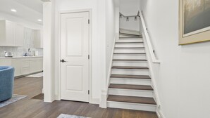 A modern interior with a staircase leading to a second floor, a kitchen area with white cabinetry, and a blue chair.