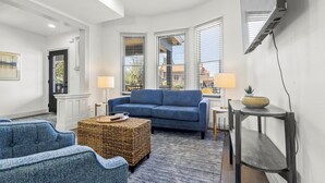 A living room with a blue sofa, two lamps, a wicker ottoman, and a TV on a wall.