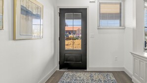 A hallway with a dark door, a framed picture on the wall, and a window with blinds.