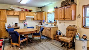 Une cuisine avec des meubles en bois, une table à manger avec des chaises, un petit îlot central et une fenêtre avec des stores.